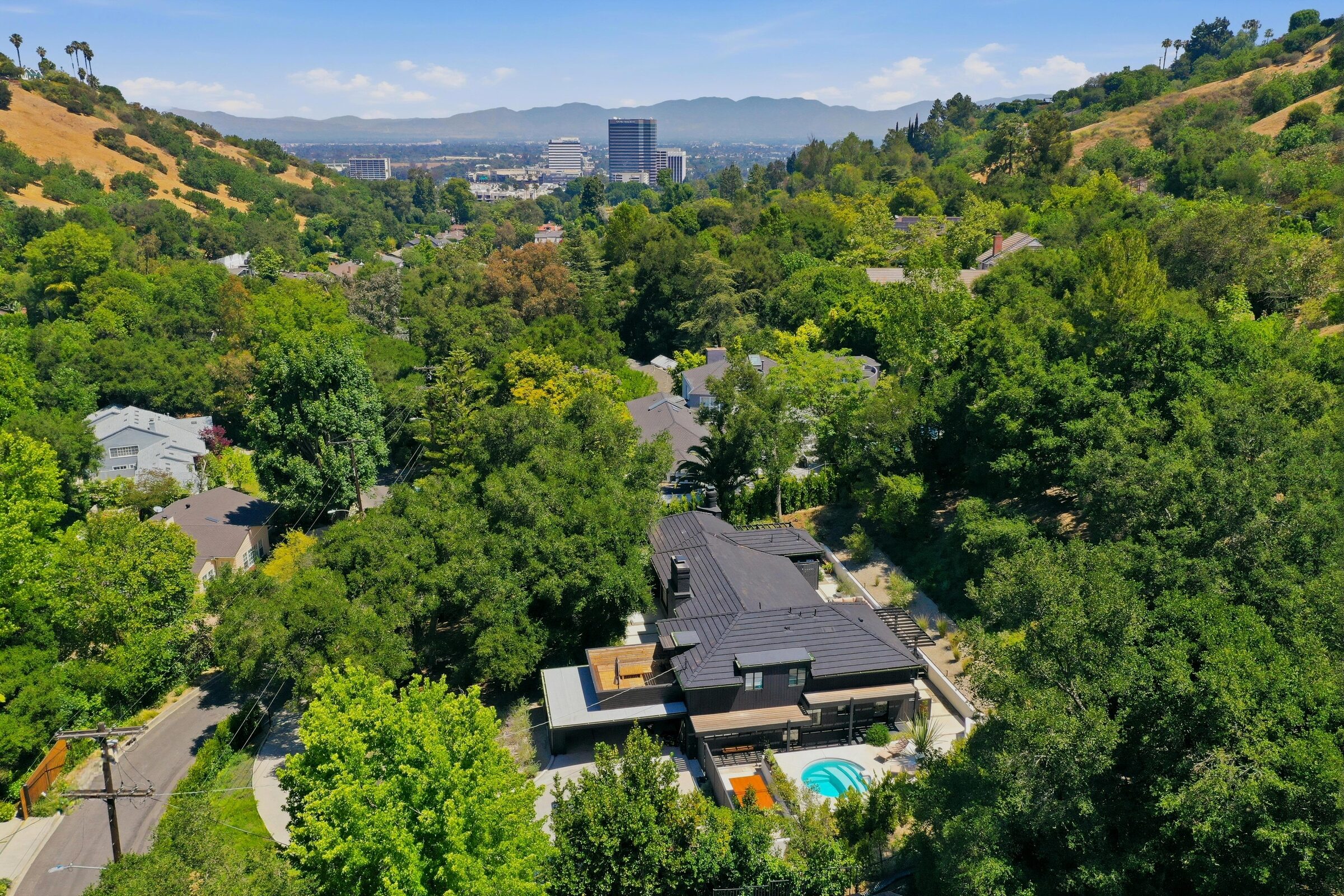Residential drone image showing a wooded hillside property and neighborhood context